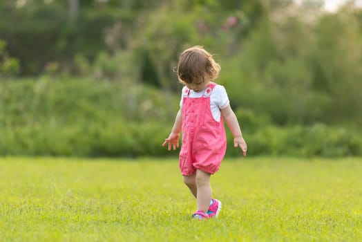playful cute little girl cheerfully spending time while running in the spacious backyard on the grass