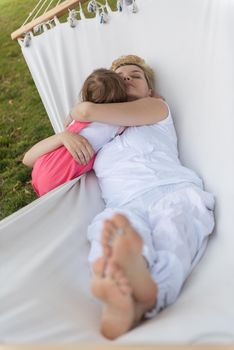 Happy mother and a little daughter enjoying free time hugging and relaxing in a hammock during a sunny day on holiday home garden