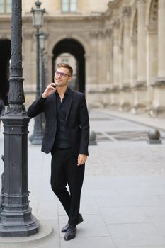 Young caucasian man in glasses walking in Paris and wearing black suit, France. Concept of walking in city and male fashion.