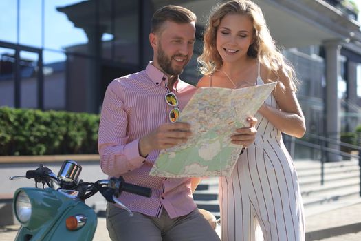 Young happy loving couple looking at map and sitting on scooter
