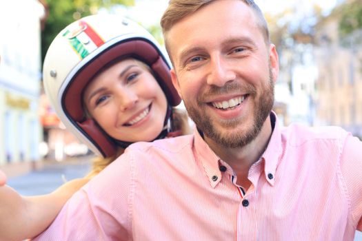 Happy young couple taking selfie while sitting on scooter outdoors
