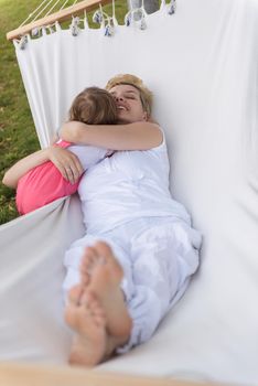 Happy mother and a little daughter enjoying free time hugging and relaxing in a hammock during a sunny day on holiday home garden