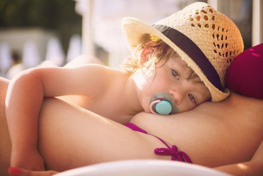 young mother and tired little daughter resting on sunbed by the pool