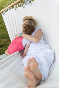 Happy mother and a little daughter enjoying free time hugging and relaxing in a hammock during a sunny day on holiday home garden