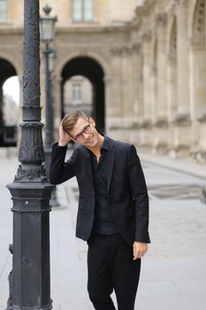 Young good looking man in glasses walking in Paris and wearing black suit, France. Concept of walking in city and male fashion.