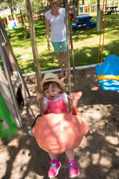 young mother and her little daughter smiling together while swinging at the playground in the park