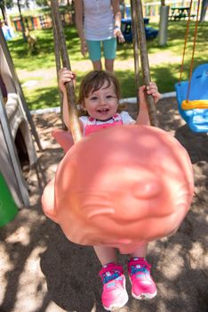 young mother and her little daughter smiling together while swinging at the playground in the park