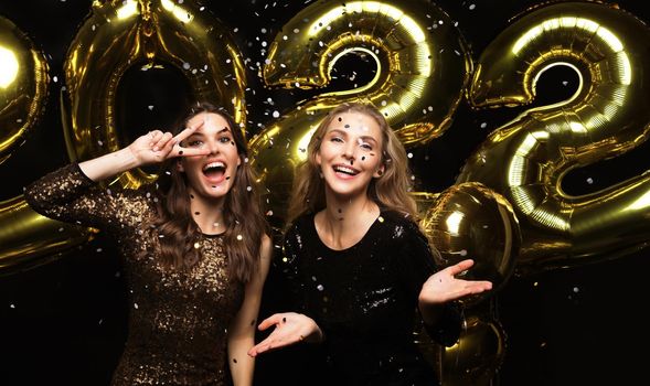 Happy gorgeous girls in stylish sexy party dresses holding gold 2022 balloons, having fun at Christmas or New Year's Eve Party