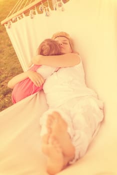 Happy mother and a little daughter enjoying free time hugging and relaxing in a hammock during a sunny day on holiday home garden