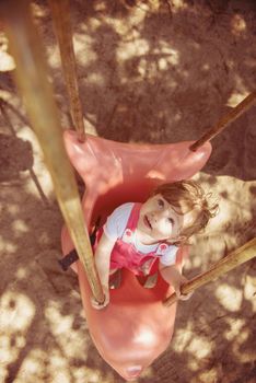 cheerful smiling cute little girl having fun while swinging  on a playground  in the park