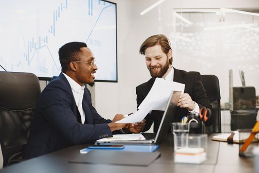 African man in a black suit. International partners. People sitting at the table with laptop.