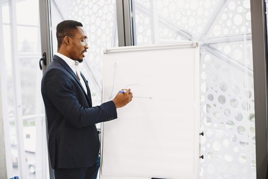 African man in a black suit. Writing board. Guy do presentation.