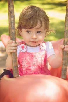 cheerful smiling cute little girl having fun while swinging  on a playground  in the park