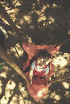 cheerful smiling cute little girl having fun while swinging  on a playground  in the park