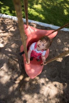 cheerful smiling cute little girl having fun while swinging  on a playground  in the park