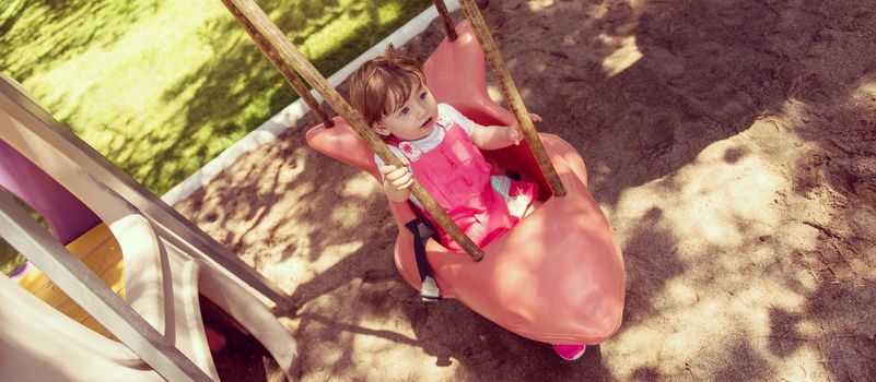 cheerful smiling cute little girl having fun while swinging  on a playground  in the park