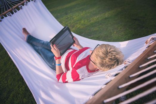 young woman using a tablet computer while relaxing on hammock in a peaceful garden during holiday