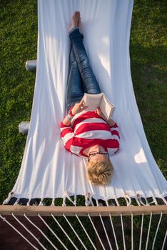 young woman reading a book while relaxing on hammock in a peaceful garden during holiday