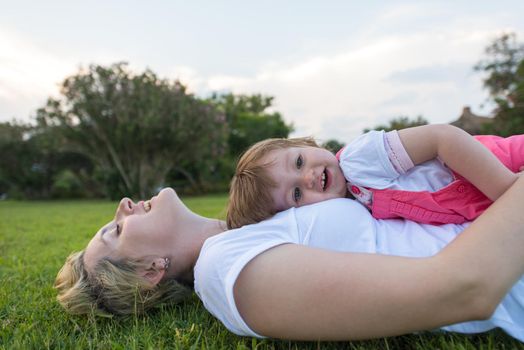 Young Mother and cute little daughter enjoying free time playing outside at backyard on the grass, happy family in nature concept