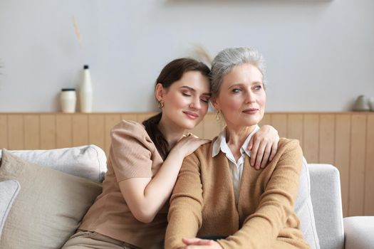 Beautiful mother and daughter. Cheerful young woman is embracing her middle aged mother in living room. Family portrait