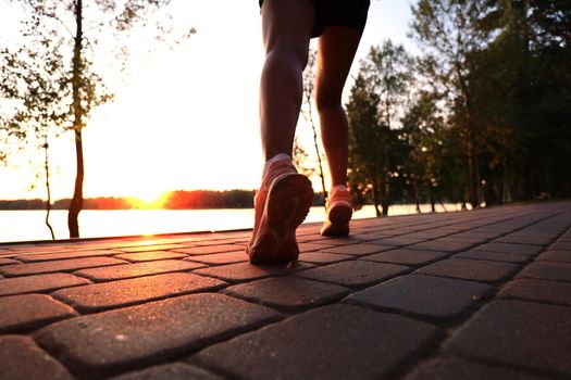 Runner feet running on road closeup on shoe, outdoor at sunset or sunrise