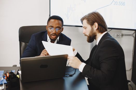 African man in a black suit. International partners. People sitting at the table with laptop.