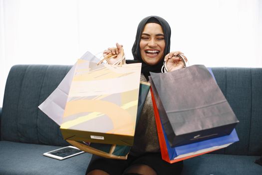 Modern arab girl in hijab at home, doing shopping online, while sitting on couch in living room.. Concept of easy online shopping.