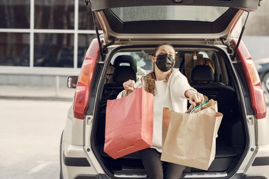 Girl on a shopping. Lady in a mask. Woman with a shopping bags. Lady near trunk of the car. Coronavirus theme.