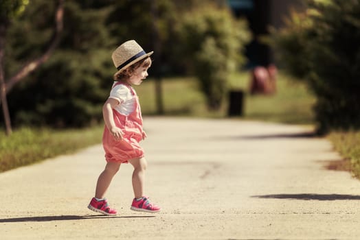 cute little girl with hat cheerfully spending time while running at Park on the summer morning