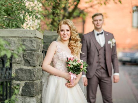 happy bride with wedding bouquet standing on city street. holidays and events