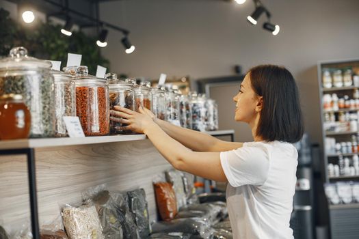 Brunette chooses food. Lady holding a jar of cinnamon. Girl in a white shirt in the supermarket.