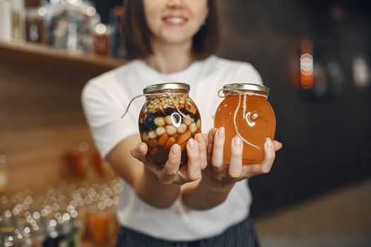 Brunette chooses food. Lady is holding jars of honey and nuts. Girl in a white shirt in the supermarket.