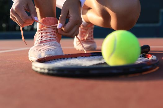 Sports woman getting ready for playing tennis tying shoelaces on outdoor