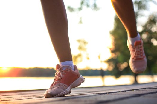 Woman runner legs and shoes in action on road outdoors at sunset