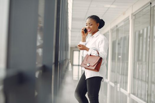 Black girl in the office. Woman in a white shirt. Lady use the phone.