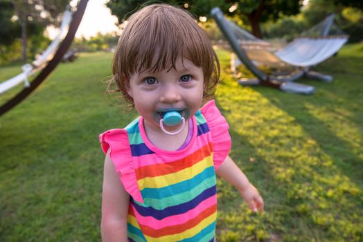 playful cute little girl cheerfully spending time while running in the spacious backyard on the grass