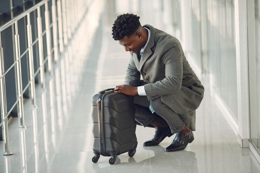 Black man at the airport. Guy with suitcase. Male in a black suit.