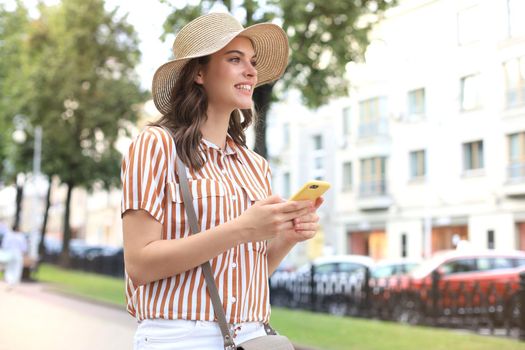 Happy beautiful young brunette girl using mobile phone while walking outdoors