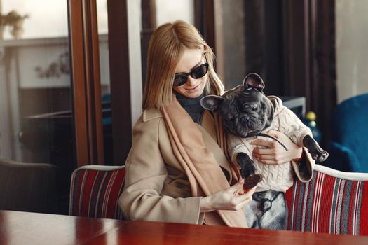 Woman with dog. Lady in a brown coat. Girl play with bulldog. Woman in a cafe.