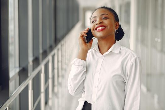 Black girl in the office. Woman in a white shirt. Lady use the phone.