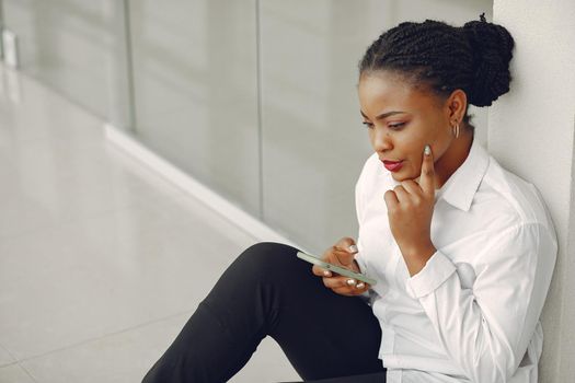 Black girl in the office. Woman in a white shirt. Lady use the phone.