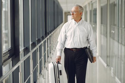 Man at the airport. Senior with suitcase. Male in a white shirt.