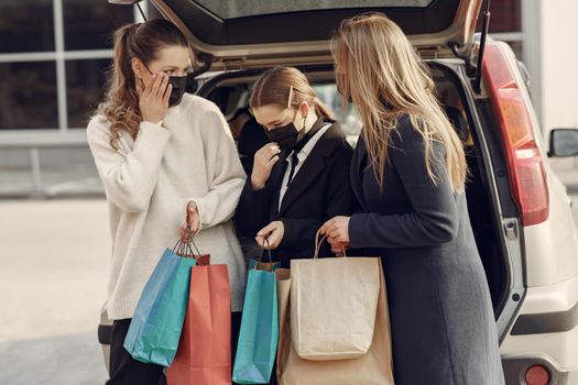 Girls on a shopping. People in a masks. Women with a shopping bags. Lady near trunk of the car. Coronavirus theme.