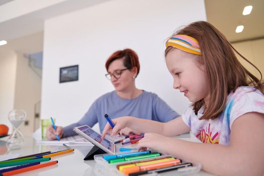 Mother and little daughter  playing together  drawing creative artwork during coronavirus quarantine measuring time on sandglass and listening music on tablet