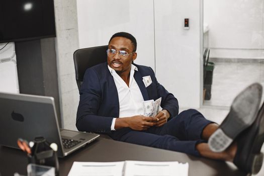 African man in a black suit. Guy sitting at the table. Businessman with money.