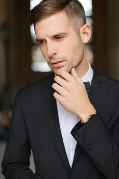 Portrait of young man wearing black suit with bow tie and white shirt. Concept of male groom model.