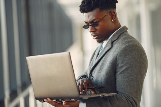 Black man in gray coat. Businessman working in a office. Guy with a laptop.