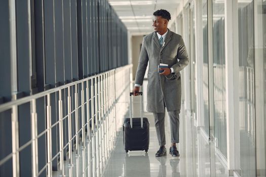 Black man at the airport. Guy with suitcase. Male in a black suit.