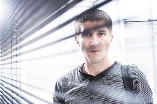 close up. serious young man looking through window blinds