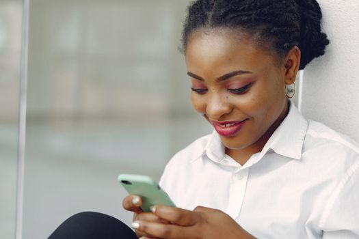 Black girl in the office. Woman in a white shirt. Lady use the phone.